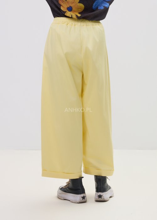 Żółte spodnie damskie z szeroką nogawką i elastycznym pasem, o luźnym, wygodnym kroju. Lekkie spodnie w pastelowym odcieniu żółci zestawione z trampkami w swobodnej, miejskiej stylizacji.