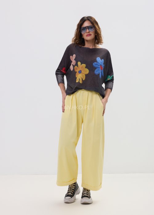 Żółte spodnie damskie z szeroką nogawką i elastycznym pasem, o luźnym, wygodnym kroju. Lekkie spodnie w pastelowym odcieniu żółci zestawione z trampkami w swobodnej, miejskiej stylizacji.