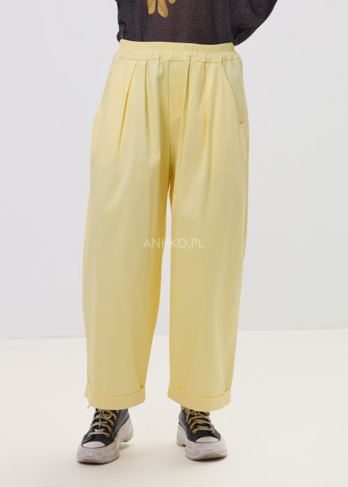 Żółte spodnie damskie z szeroką nogawką i elastycznym pasem, o luźnym, wygodnym kroju. Lekkie spodnie w pastelowym odcieniu żółci zestawione z trampkami w swobodnej, miejskiej stylizacji.