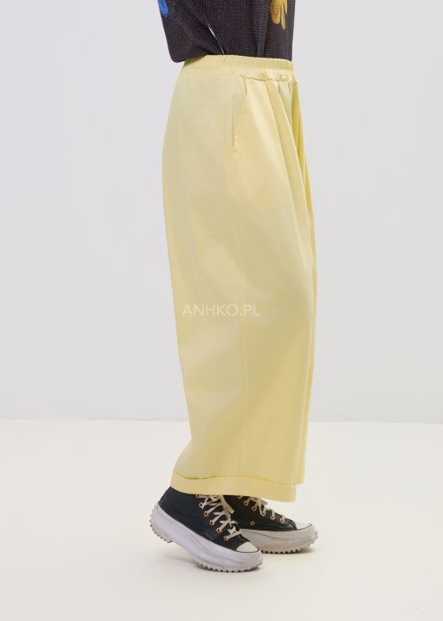 Żółte spodnie damskie z szeroką nogawką i elastycznym pasem, o luźnym, wygodnym kroju. Lekkie spodnie w pastelowym odcieniu żółci zestawione z trampkami w swobodnej, miejskiej stylizacji.