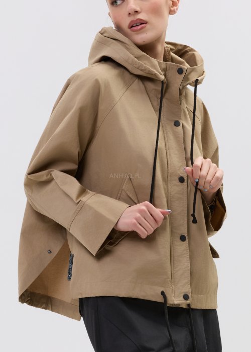 Camelowa kurtka damska z kapturem w stylu oversize, zapinana na napy, z regulacją w pasie i dużymi kieszeniami. Lekka kurtka o nowoczesnym kroju, zestawiona z czarnymi spodniami cargo.