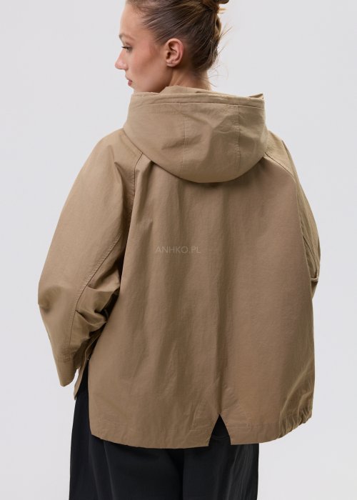 Camelowa kurtka damska z kapturem w stylu oversize, zapinana na napy, z regulacją w pasie i dużymi kieszeniami. Lekka kurtka o nowoczesnym kroju, zestawiona z czarnymi spodniami cargo.