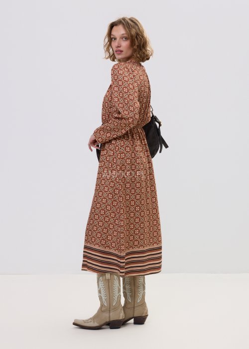 Wzorzysta sukienka midi z wiskozy w retro print w odcieniach brązu, z marszczonym dekoltem i gumką w pasie. Stylizacja z jasnymi kowbojkami i czarną torebką podkreśla modowy charakter modelu.