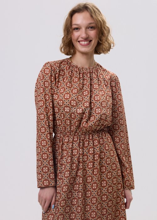 Wzorzysta sukienka midi z wiskozy w retro print w odcieniach brązu, z marszczonym dekoltem i gumką w pasie. Stylizacja z jasnymi kowbojkami i czarną torebką podkreśla modowy charakter modelu.