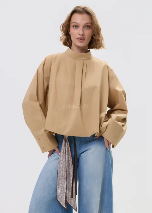 Beżowa bluzka damska oversize z wysoką stójką i szerokimi rękawami, minimalistyczny fason zestawiony z jasnymi jeansami w casualowej stylizacji.