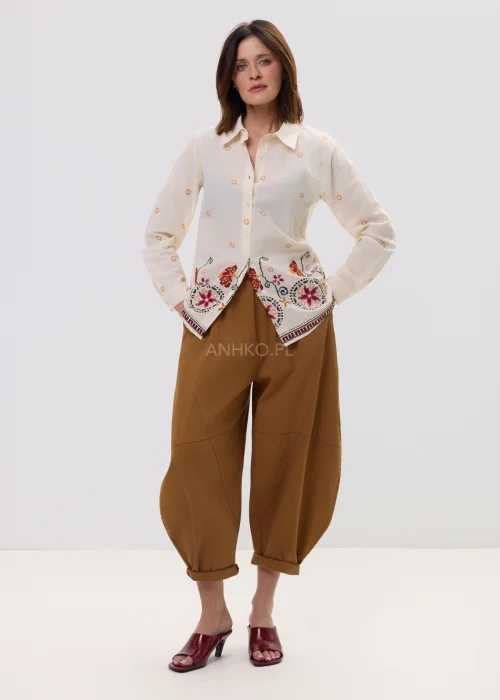 Kremowa koszula damska z delikatnym haftem kwiatowym i kolorową bordiurą u dołu, o lekkim, przewiewnym materiale i klasycznym kołnierzyku.