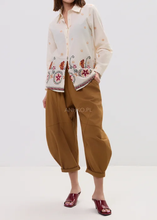 Kremowa koszula damska z delikatnym haftem kwiatowym i kolorową bordiurą u dołu, o lekkim, przewiewnym materiale i klasycznym kołnierzyku.