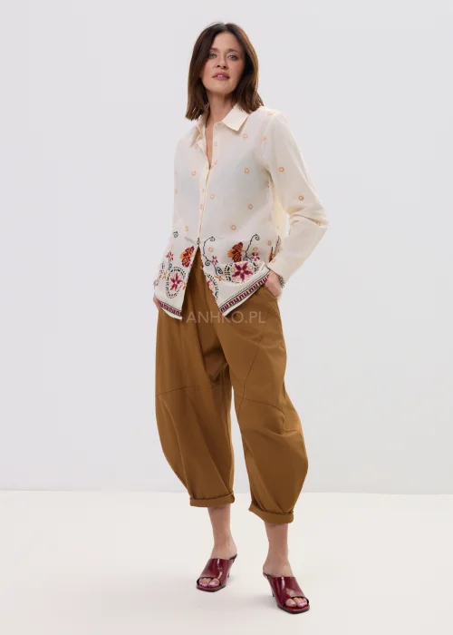 Kremowa koszula damska z delikatnym haftem kwiatowym i kolorową bordiurą u dołu, o lekkim, przewiewnym materiale i klasycznym kołnierzyku.