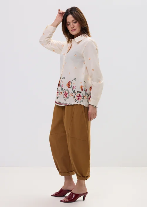 Kremowa koszula damska z delikatnym haftem kwiatowym i kolorową bordiurą u dołu, o lekkim, przewiewnym materiale i klasycznym kołnierzyku.
