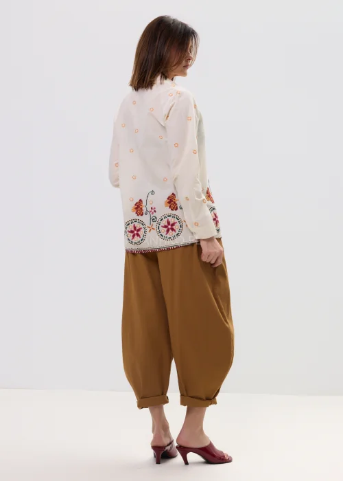 Kremowa koszula damska z delikatnym haftem kwiatowym i kolorową bordiurą u dołu, o lekkim, przewiewnym materiale i klasycznym kołnierzyku.