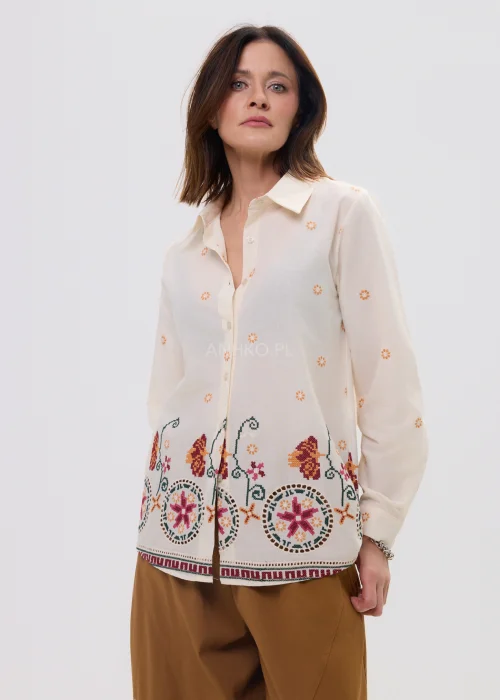 Kremowa koszula damska z delikatnym haftem kwiatowym i kolorową bordiurą u dołu, o lekkim, przewiewnym materiale i klasycznym kołnierzyku.