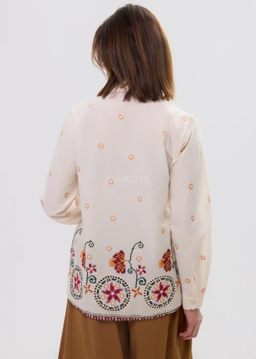 Kremowa koszula damska z delikatnym haftem kwiatowym i kolorową bordiurą u dołu, o lekkim, przewiewnym materiale i klasycznym kołnierzyku.