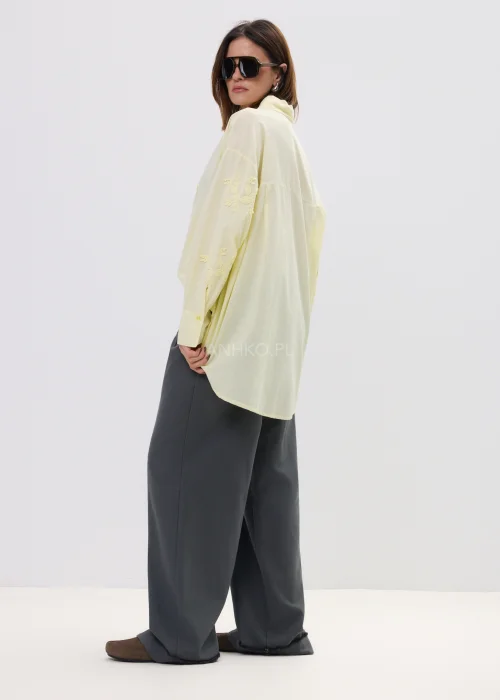 Koszula damska oversize w pastelowym żółtym kolorze, lekka transparentna tkanina z haftowanymi detalami – elegancka stylizacja ze spodniami.