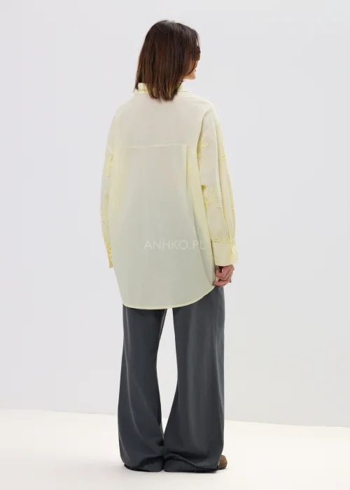Koszula damska oversize w pastelowym żółtym kolorze, lekka transparentna tkanina z haftowanymi detalami – elegancka stylizacja ze spodniami.