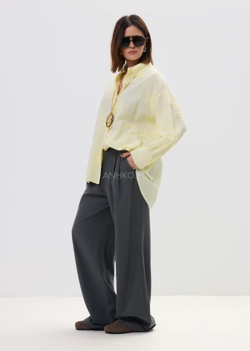 Koszula damska oversize w pastelowym żółtym kolorze, lekka transparentna tkanina z haftowanymi detalami – elegancka stylizacja ze spodniami.