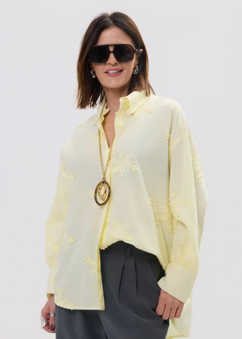 Koszula damska oversize w pastelowym żółtym kolorze, lekka transparentna tkanina z haftowanymi detalami – elegancka stylizacja ze spodniami.