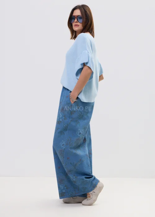 Jasnoniebieska bluzka damska z miękkiej dzianiny, o luźnym fasonie i krótkim rękawie z falbaną, z dekoltem w kształcie litery V. Lekki materiał i swobodny krój podkreślają casualowy, nowoczesny styl.