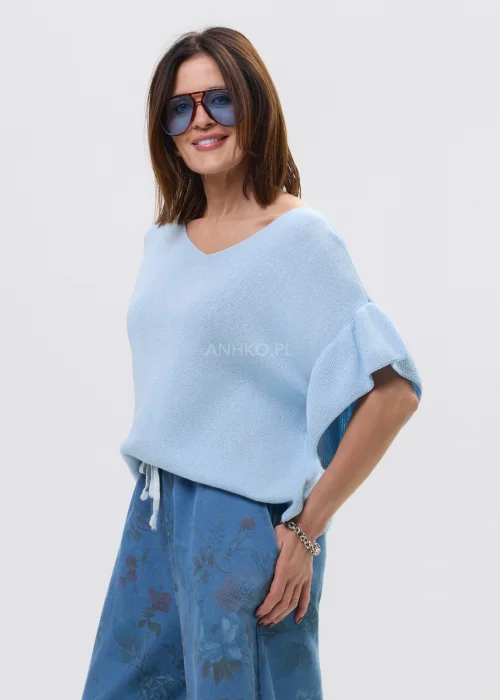 Jasnoniebieska bluzka damska z miękkiej dzianiny, o luźnym fasonie i krótkim rękawie z falbaną, z dekoltem w kształcie litery V. Lekki materiał i swobodny krój podkreślają casualowy, nowoczesny styl.
