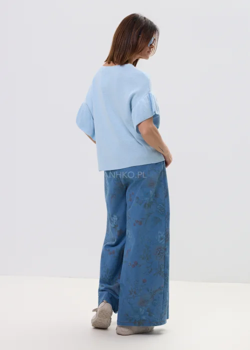 Jasnoniebieska bluzka damska z miękkiej dzianiny, o luźnym fasonie i krótkim rękawie z falbaną, z dekoltem w kształcie litery V. Lekki materiał i swobodny krój podkreślają casualowy, nowoczesny styl.