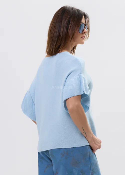 Jasnoniebieska bluzka damska z miękkiej dzianiny, o luźnym fasonie i krótkim rękawie z falbaną, z dekoltem w kształcie litery V. Lekki materiał i swobodny krój podkreślają casualowy, nowoczesny styl.