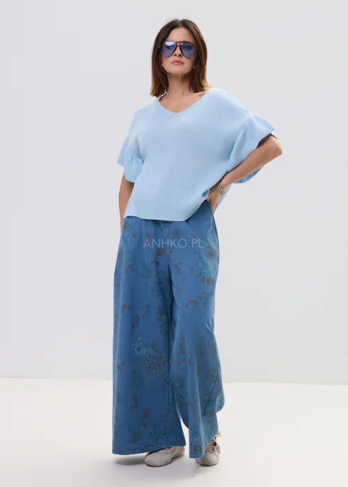 Jasnoniebieska bluzka damska z miękkiej dzianiny, o luźnym fasonie i krótkim rękawie z falbaną, z dekoltem w kształcie litery V. Lekki materiał i swobodny krój podkreślają casualowy, nowoczesny styl.