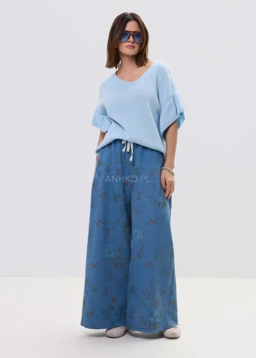 Jasnoniebieska bluzka damska z miękkiej dzianiny, o luźnym fasonie i krótkim rękawie z falbaną, z dekoltem w kształcie litery V. Lekki materiał i swobodny krój podkreślają casualowy, nowoczesny styl.