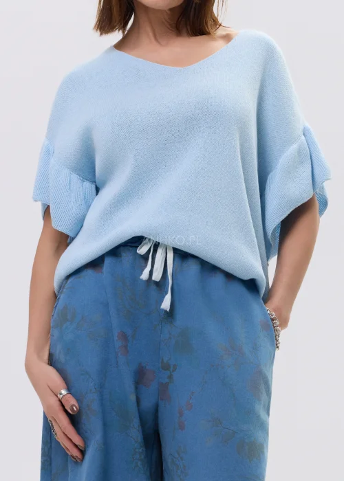Jasnoniebieska bluzka damska z miękkiej dzianiny, o luźnym fasonie i krótkim rękawie z falbaną, z dekoltem w kształcie litery V. Lekki materiał i swobodny krój podkreślają casualowy, nowoczesny styl.
