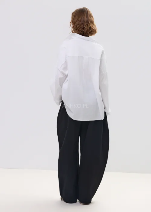 Biała koszula damska oversize z długim rękawem i klasycznym kołnierzykiem, luźny fason, minimalistyczna stylizacja.