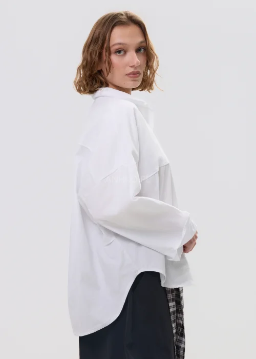 Biała koszula damska oversize z długim rękawem i klasycznym kołnierzykiem, luźny fason, minimalistyczna stylizacja.