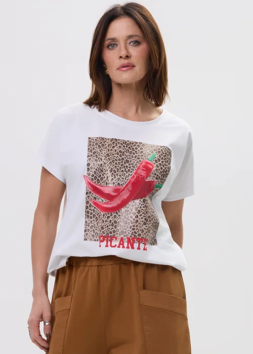 Biały t-shirt z nadrukiem czerwonych papryczek na tle panterki i napisem „PICANTE”, luźny fason – stylizacja z brązowymi spodniami.
