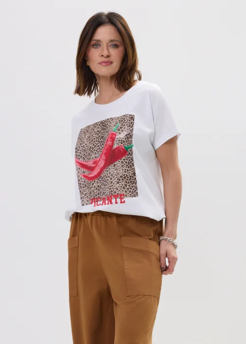 Biały t-shirt z nadrukiem czerwonych papryczek na tle panterki i napisem „PICANTE”, luźny fason – stylizacja z brązowymi spodniami.