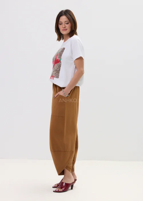 Biały t-shirt z nadrukiem czerwonych papryczek na tle panterki i napisem „PICANTE”, luźny fason – stylizacja z brązowymi spodniami.