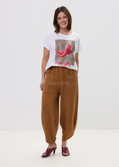 Biały t-shirt z nadrukiem czerwonych papryczek na tle panterki i napisem „PICANTE”, luźny fason – stylizacja z brązowymi spodniami.