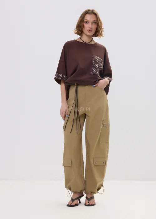 Brązowa bluzka oversize z krótkim rękawem, kieszonka i mankiety zdobione ćwiekami, casualowa stylizacja.