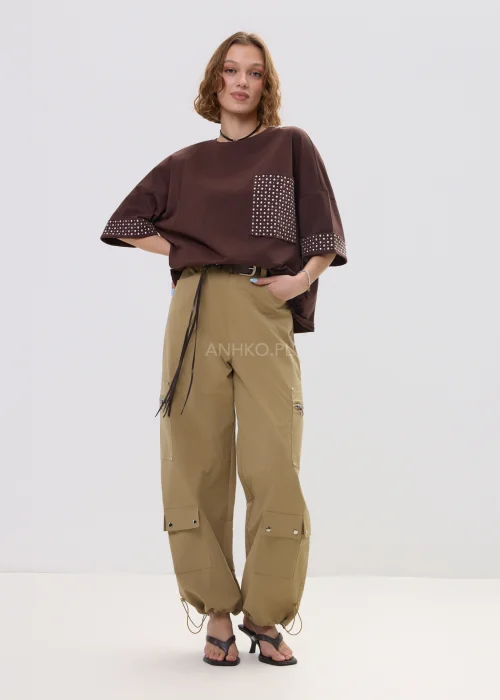 Brązowa bluzka oversize z krótkim rękawem, kieszonka i mankiety zdobione ćwiekami, casualowa stylizacja.