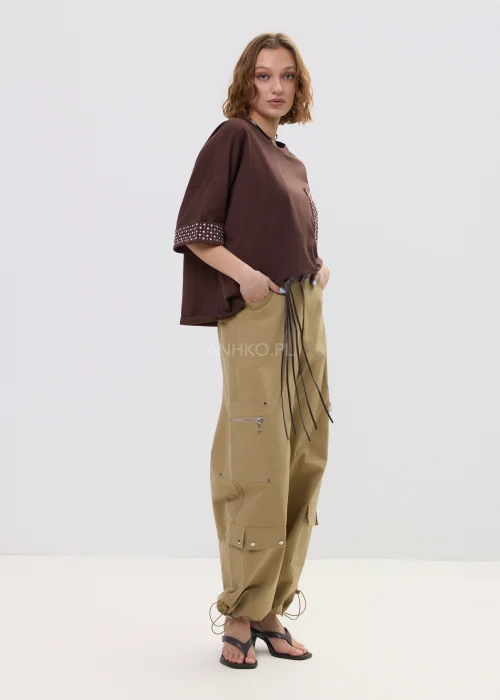 Brązowa bluzka oversize z krótkim rękawem, kieszonka i mankiety zdobione ćwiekami, casualowa stylizacja.