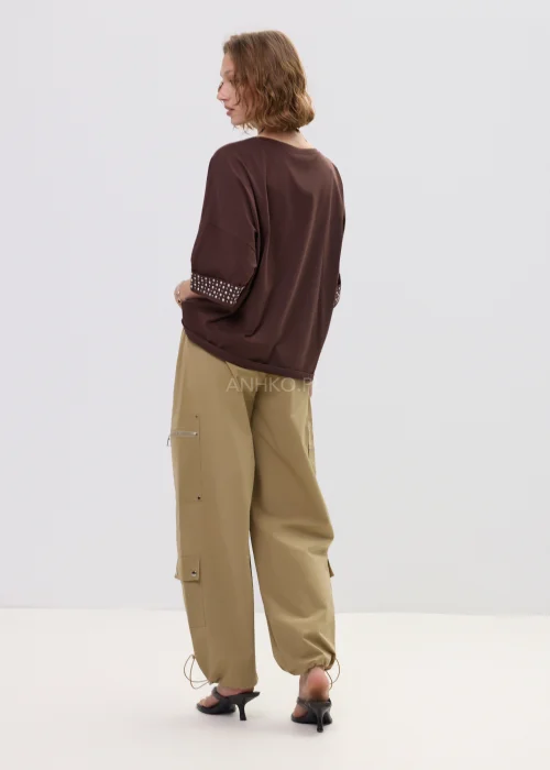 Brązowa bluzka oversize z krótkim rękawem, kieszonka i mankiety zdobione ćwiekami, casualowa stylizacja.