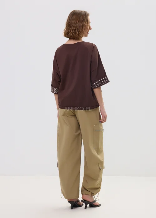 Brązowa bluzka oversize z krótkim rękawem, kieszonka i mankiety zdobione ćwiekami, casualowa stylizacja.