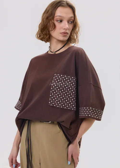 Brązowa bluzka oversize z krótkim rękawem, kieszonka i mankiety zdobione ćwiekami, casualowa stylizacja.