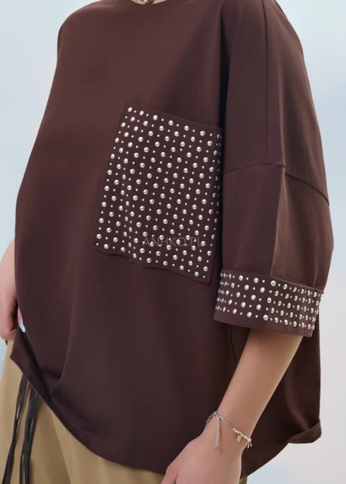 Brązowa bluzka oversize z krótkim rękawem, kieszonka i mankiety zdobione ćwiekami, casualowa stylizacja.