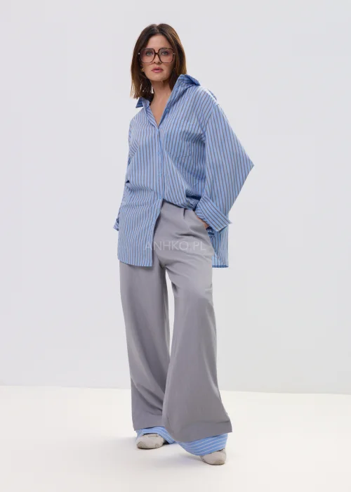 Koszula oversize w niebieskie paski z kołnierzykiem i zapięciem na guziki, luźny fason – stylizacja z eleganckimi spodniami i okularami przeciwsłonecznymi.