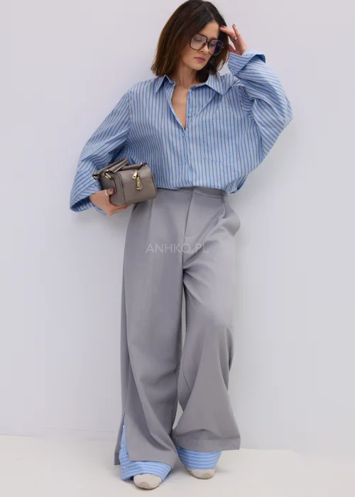 Koszula oversize w niebieskie paski z kołnierzykiem i zapięciem na guziki, luźny fason – stylizacja z eleganckimi spodniami i okularami przeciwsłonecznymi.