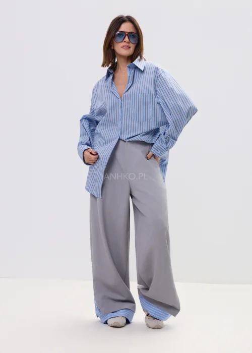 Koszula oversize w niebieskie paski z kołnierzykiem i zapięciem na guziki, luźny fason – stylizacja z eleganckimi spodniami i okularami przeciwsłonecznymi.