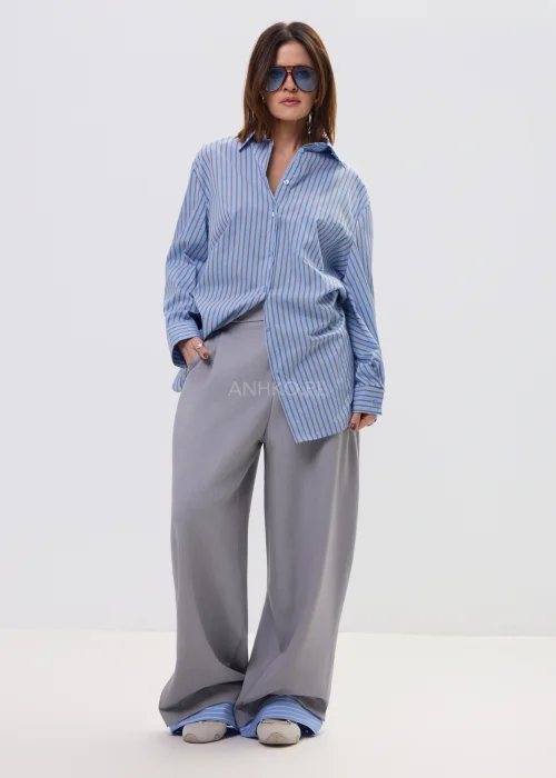 Koszula oversize w niebieskie paski z kołnierzykiem i zapięciem na guziki, luźny fason – stylizacja z eleganckimi spodniami i okularami przeciwsłonecznymi.