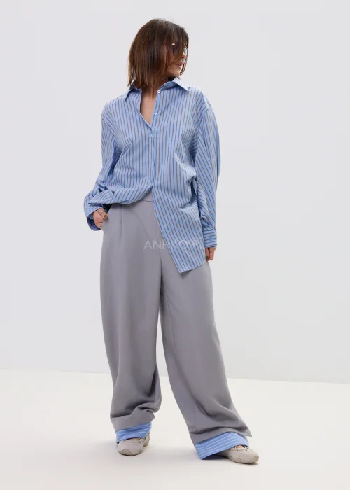 Koszula oversize w niebieskie paski z kołnierzykiem i zapięciem na guziki, luźny fason – stylizacja z eleganckimi spodniami i okularami przeciwsłonecznymi.