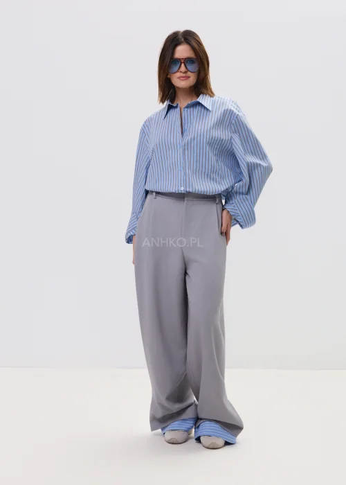 Koszula oversize w niebieskie paski z kołnierzykiem i zapięciem na guziki, luźny fason – stylizacja z eleganckimi spodniami i okularami przeciwsłonecznymi.