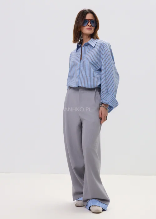Koszula oversize w niebieskie paski z kołnierzykiem i zapięciem na guziki, luźny fason – stylizacja z eleganckimi spodniami i okularami przeciwsłonecznymi.