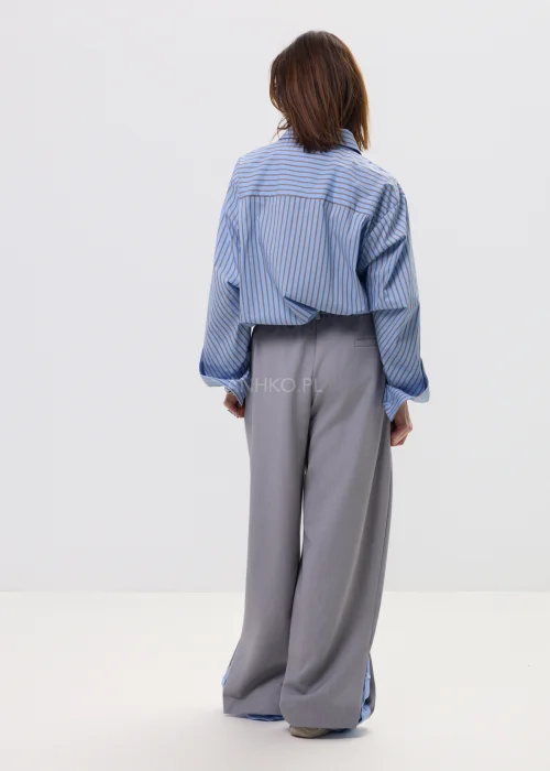 Koszula oversize w niebieskie paski z kołnierzykiem i zapięciem na guziki, luźny fason – stylizacja z eleganckimi spodniami i okularami przeciwsłonecznymi.