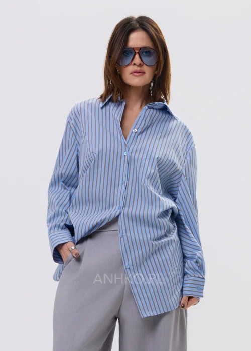 Koszula oversize w niebieskie paski z kołnierzykiem i zapięciem na guziki, luźny fason – stylizacja z eleganckimi spodniami i okularami przeciwsłonecznymi.