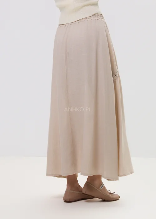 Beżowa spódnica maxi z elastyczną talią i dekoracyjnymi marszczeniami, lekki materiał, asymetryczne przeszycia – stylizacja z balerinami.